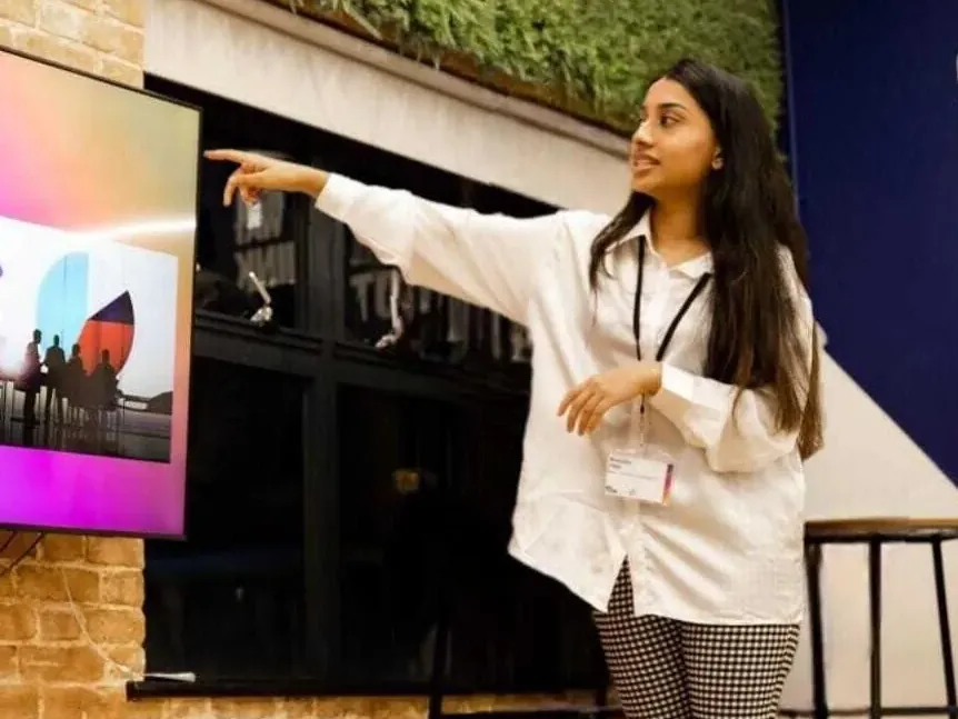 Bhavisha presenting, pointing at a screen as she speaks to a room.